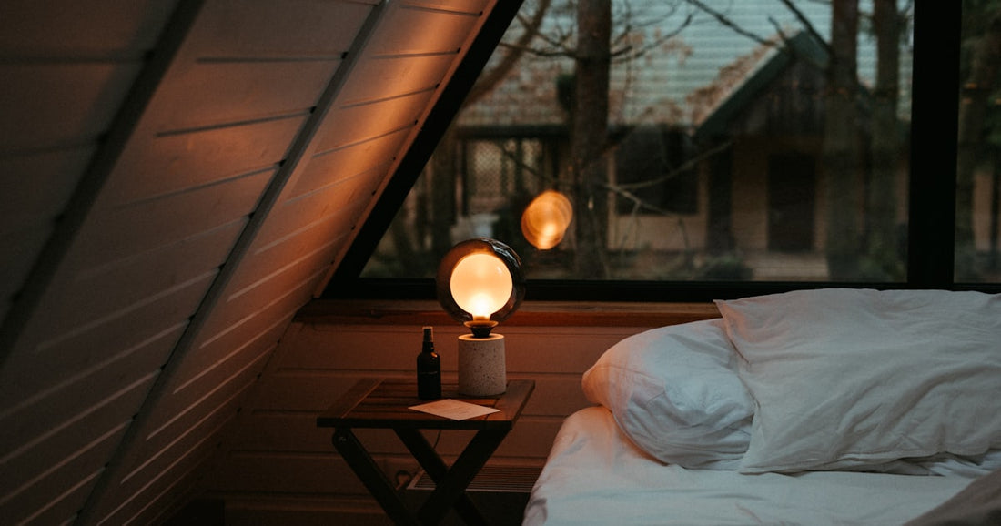 Cozy small bedroom with warm light, a bed beneath a window and a nightstand